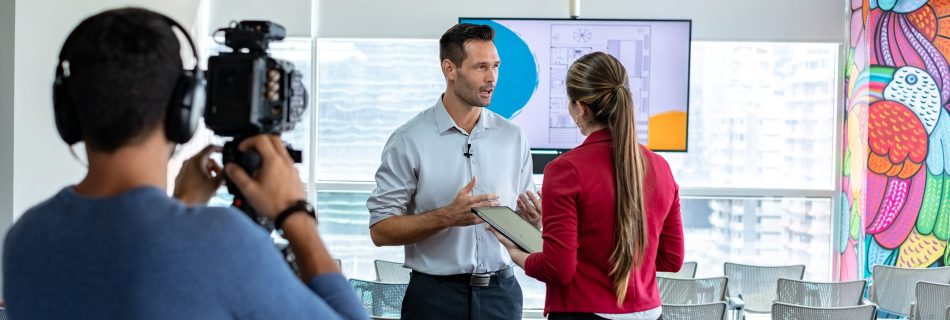 Illustration of a professional video shoot in a modern office with a camera filming two people in a business meeting.